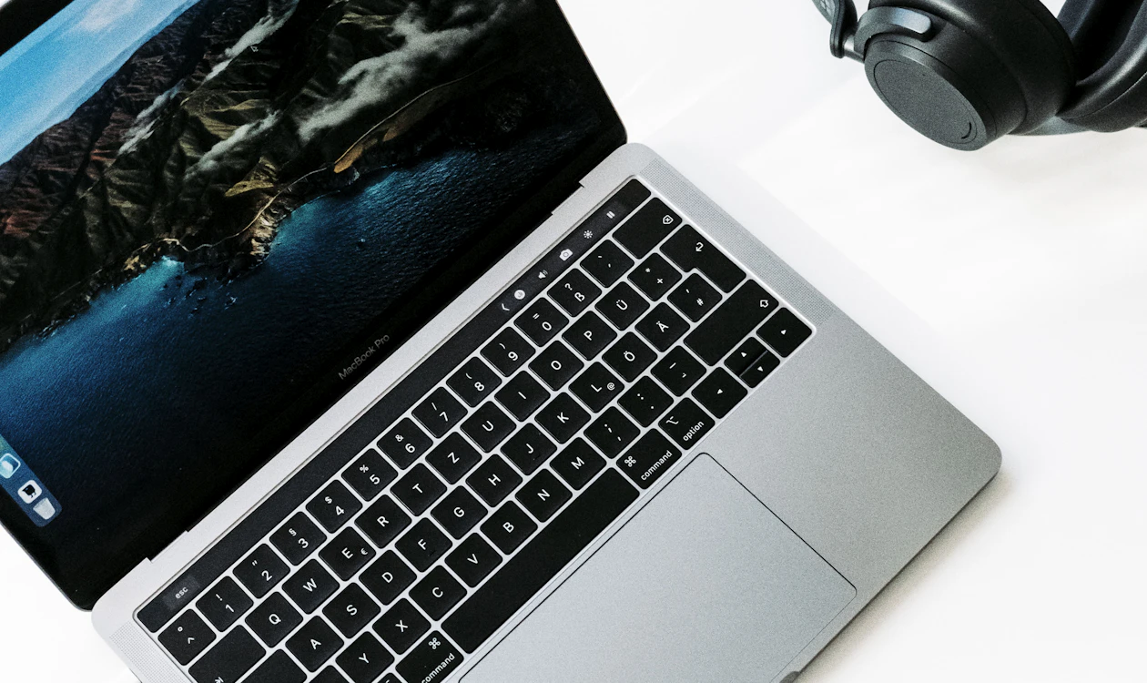 Laptop beside black headphones on a white desk
